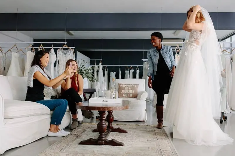Woman trying on wedding dress in a shop with friends-cm (1)